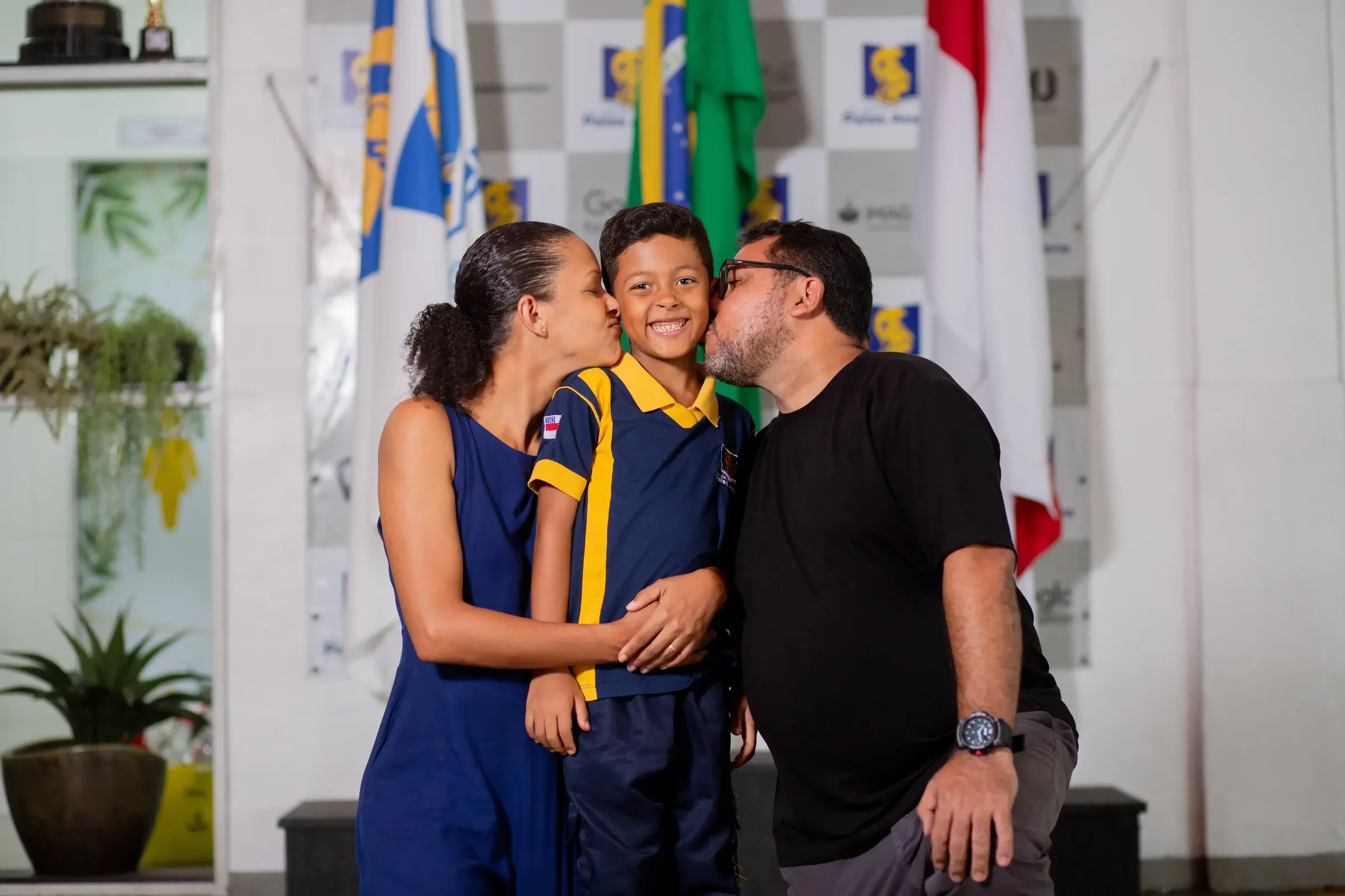 Família e aluno uniformizado do Palas Atena diante das bandeiras