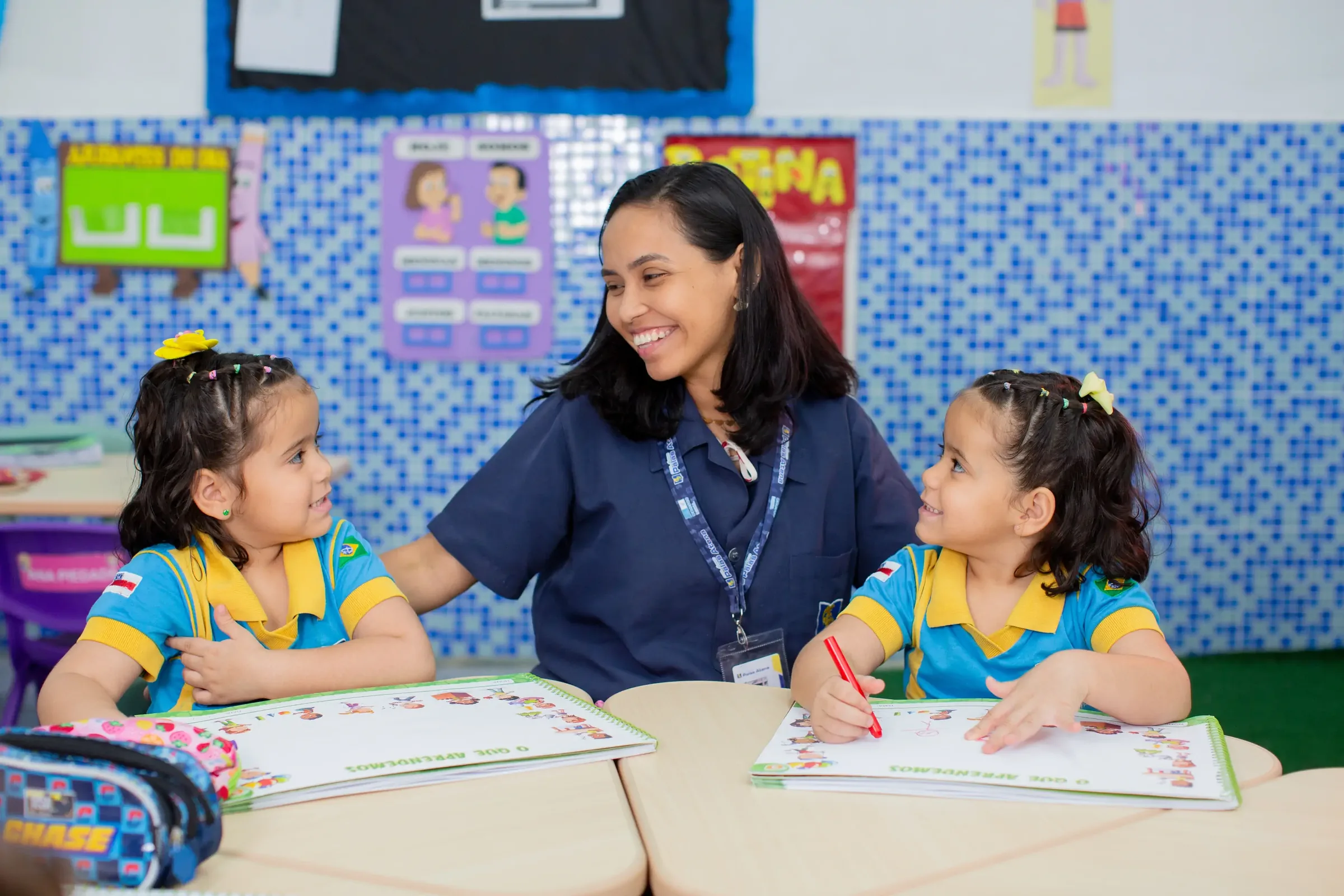 Professora do Palas Atena sorrindo com duas alunas da educação infantil