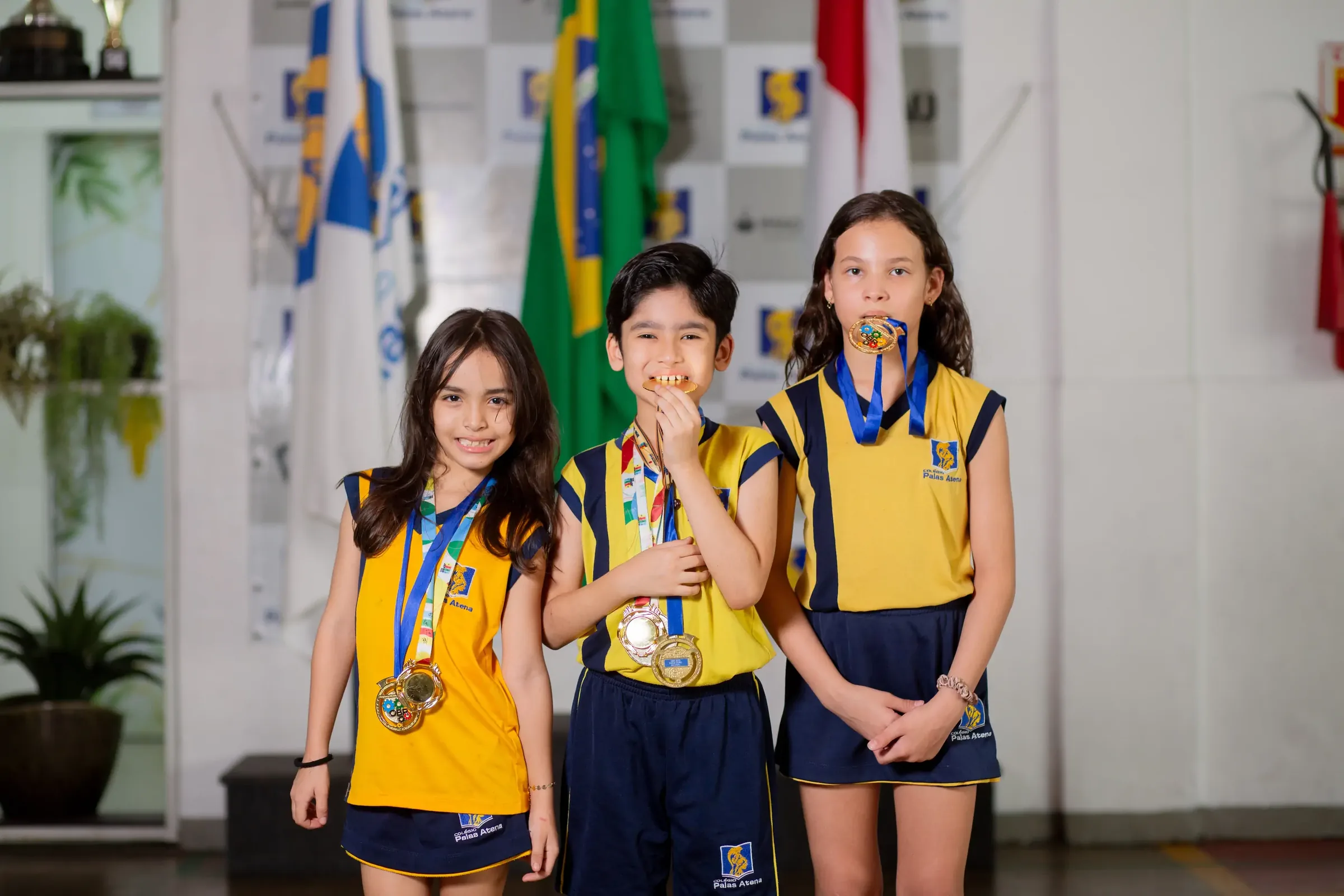 Três alunos do Palas Atena com medalhas diante das bandeiras