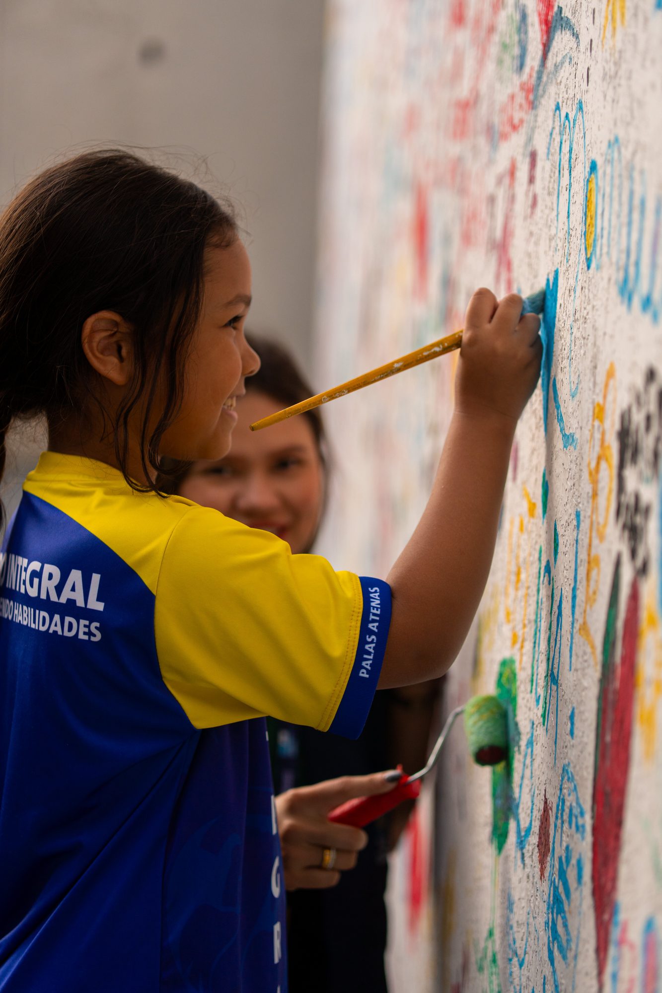 Aluna do Palas Atena pintando o muro da escola